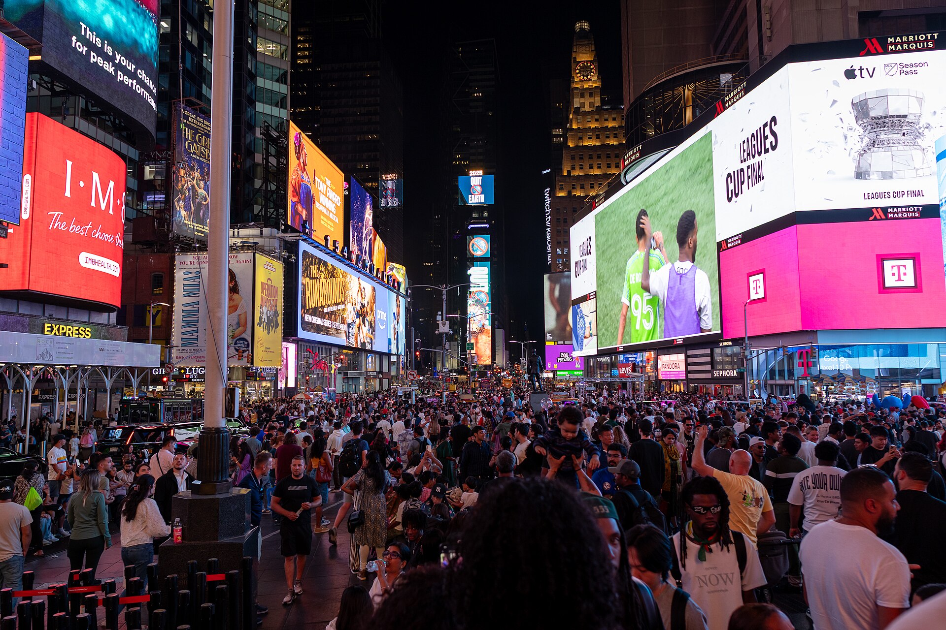 City square at night with large LED screens on the buildings and a crowd below